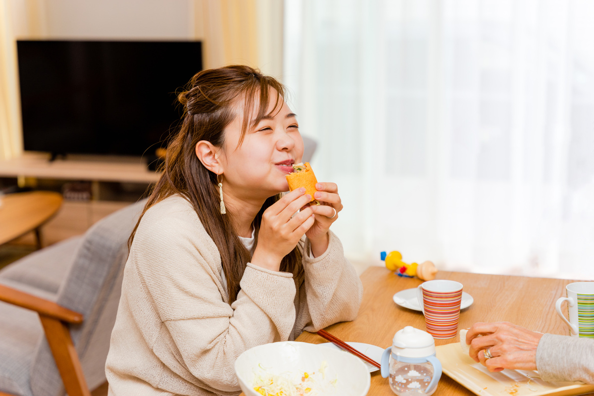 A woman in her 20s to 30s smiling to eat burritos in her living room